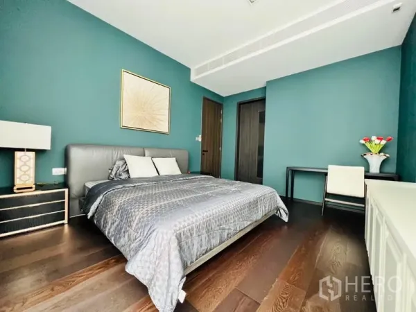 Condominium for rent in Watthana, Bangkok - Primary bedroom with teal accent walls, king bed, dark wood floors, desk and bedside tables.