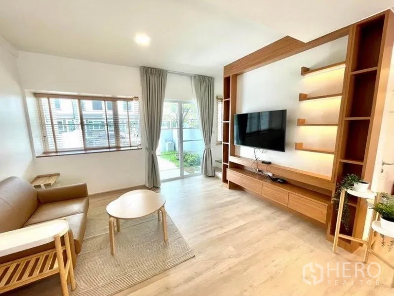 ทาวน์เฮาส์ ให้เช่าในPrawet, Bangkok - ห้องนั่งเล่นมีผนังทีวี หน้าต่างบานใหญ่ และประตูกระจกสไลด์ออกสู่สวน