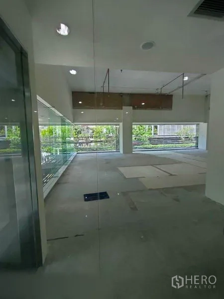 零售空间 出租在Khlong Toei, Bangkok - 明亮的空置商铺，落地窗与外部绿景，高挑裸顶。