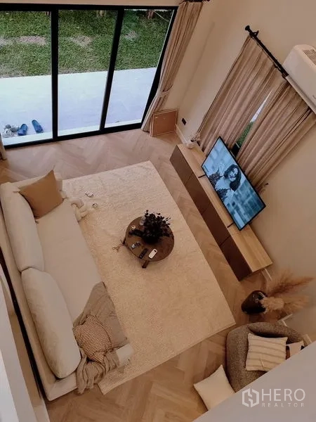 บ้าน ให้เช่าในKhlong Toei, Bangkok - ห้องรับแขกเพดานสูง พื้นไม้ลายก้างปลา พรมใหญ่ โซฟา และประตูกระจกเปิดสู่สวน