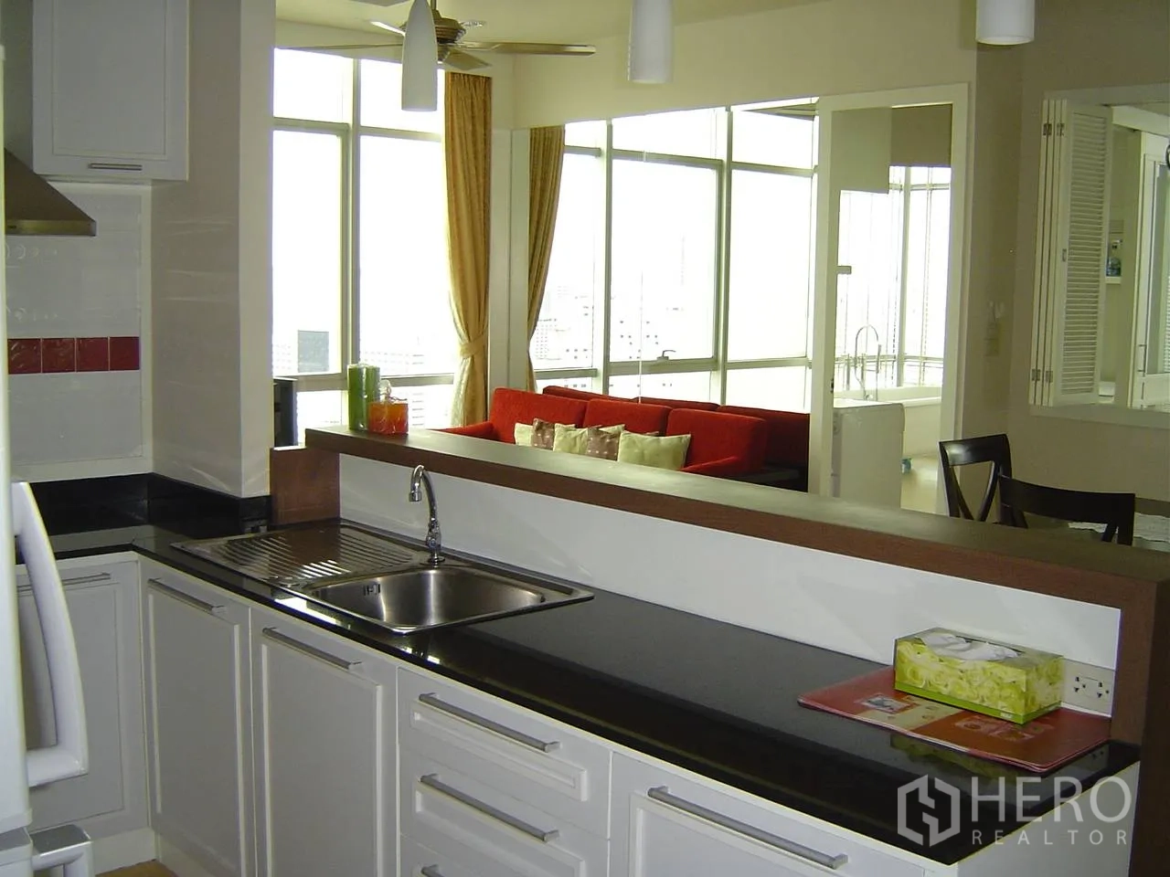 公寓 出租在Khlong San, Bangkok - 开放式厨房，白色橱柜与黑色台面，面向采光良好的客厅与河景。