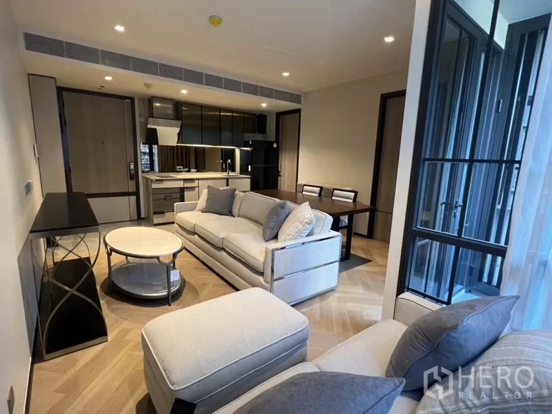 คอนโด ให้เช่าในKhlong Toei, Bangkok - ห้องนั่งเล่นแบบโอเพ่นแพลน โซฟาสีอ่อน พื้นลายก้างปลา และครัวยูนิตกะทัดรัดตู้สีเข้ม