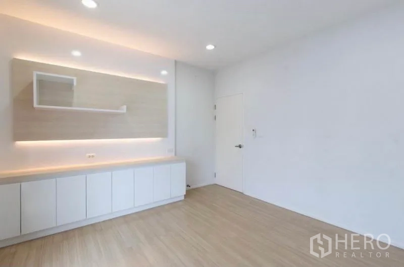 Townhouse for rent or sale in Watthana, Bangkok - Minimal living area with built-in white cabinets and warm LED accent lighting.