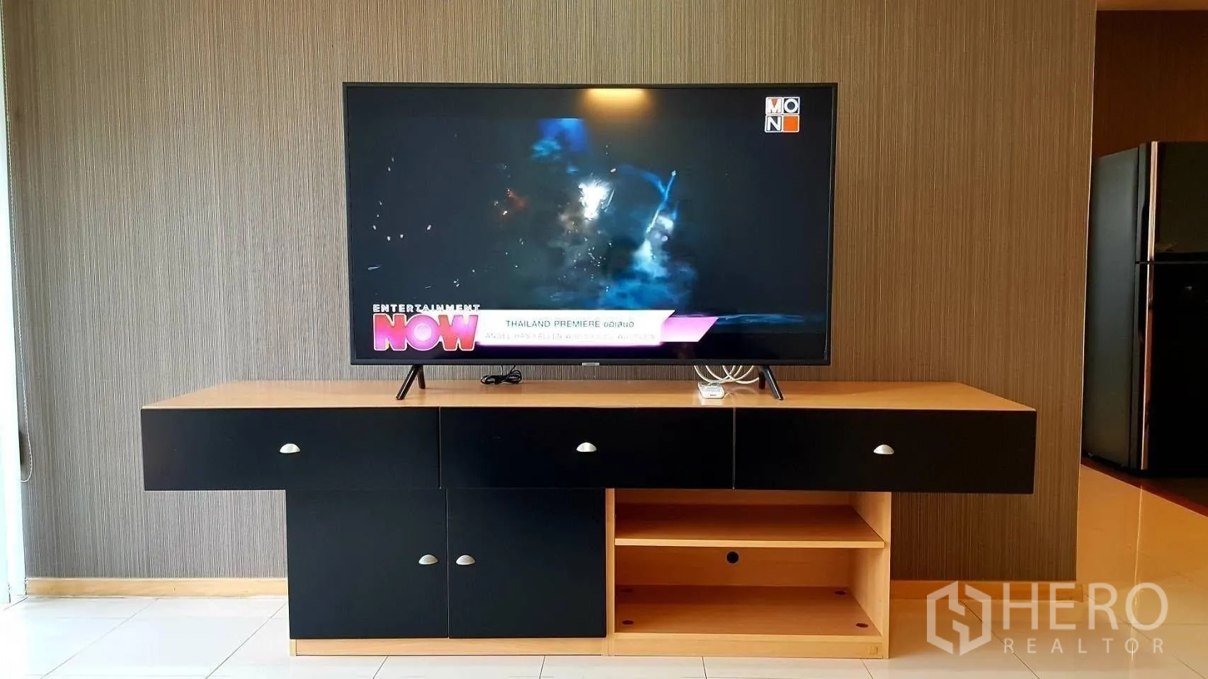 Condominium for rent in Khlong Toei, Bangkok - Living room TV on a wood-and-black console against a textured wall.