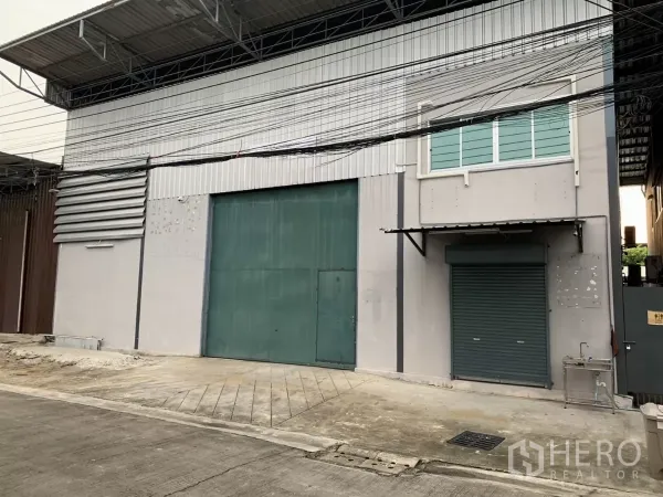 货栈 出租在Bang Kapi, Bangkok - 仓库外观，带大型绿色推拉门、卷闸门与有顶装卸区