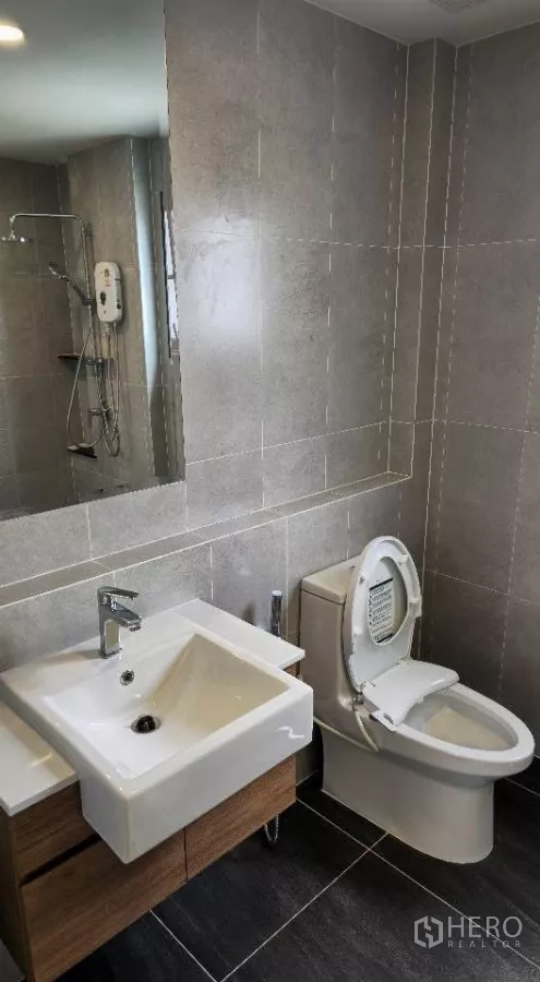 Detached House for rent or sale in Bang Phli, Samut Prakan - Modern bathroom with square basin vanity, toilet and glass shower with electric heater on gray tiles.