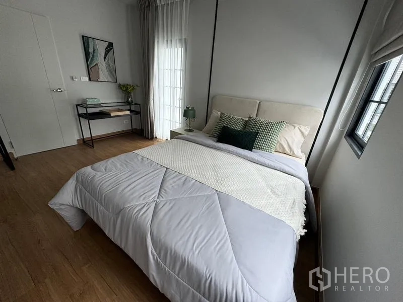 Detached House for rent or sale in Bang Phli, Samut Prakan - Sunlit bedroom with light bedding, corner console table and balcony door.