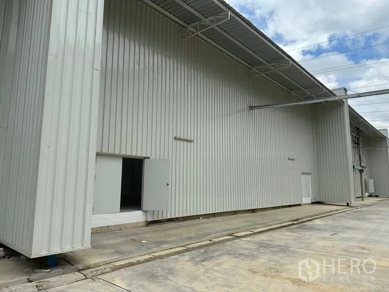 Factory for rent in Khlong Luang, Pathum Thani - Side view of the corrugated metal warehouse exterior with service doors and covered eaves