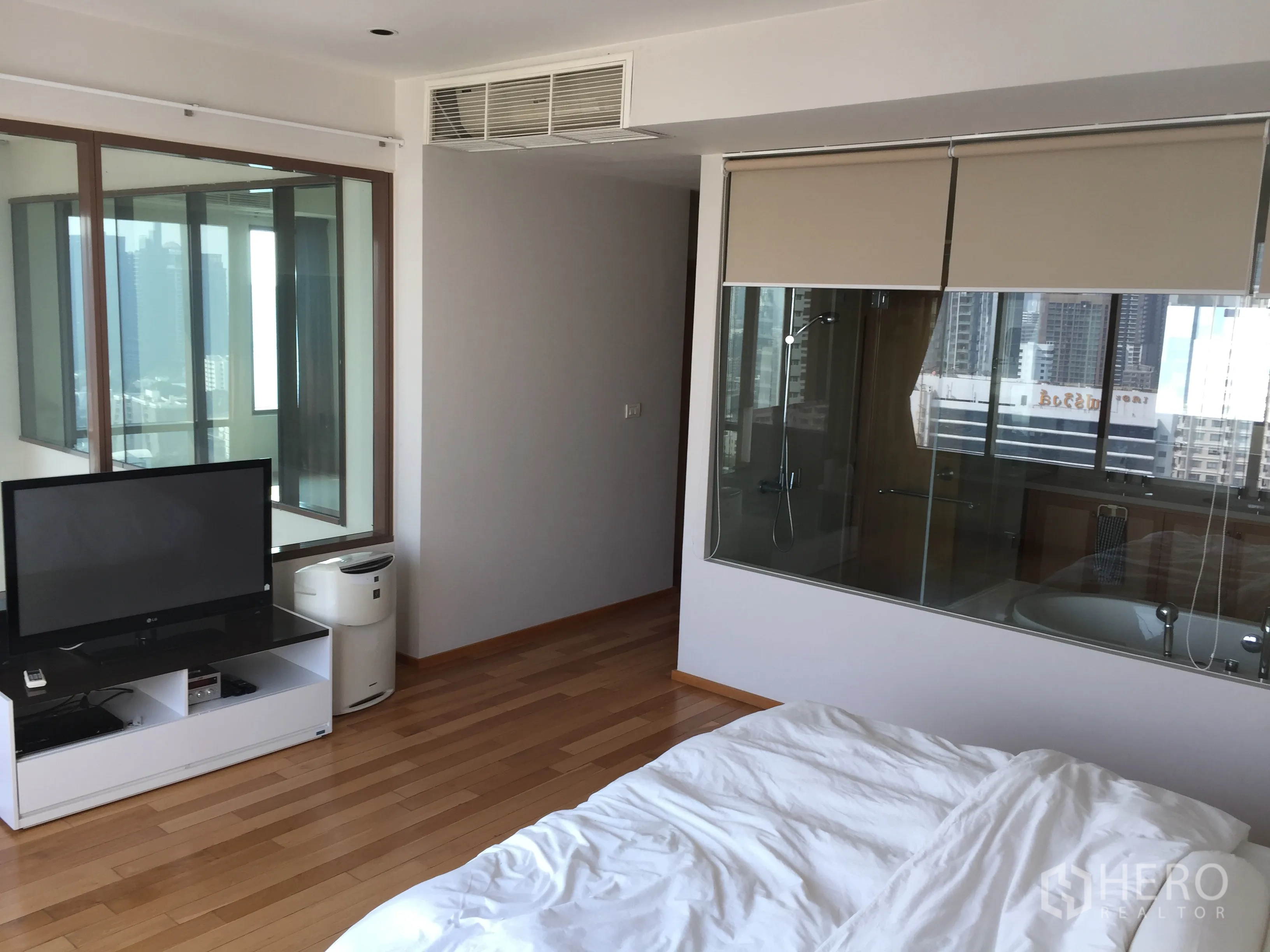 คอนโด ให้เช่าหรือขายในKhlong Toei, Bangkok - ห้องนอนมาสเตอร์พร้อมชั้นวางทีวี พื้นไม้ และผนังกระจกเชื่อมห้องน้ำในตัวมองเห็นวิวเมือง