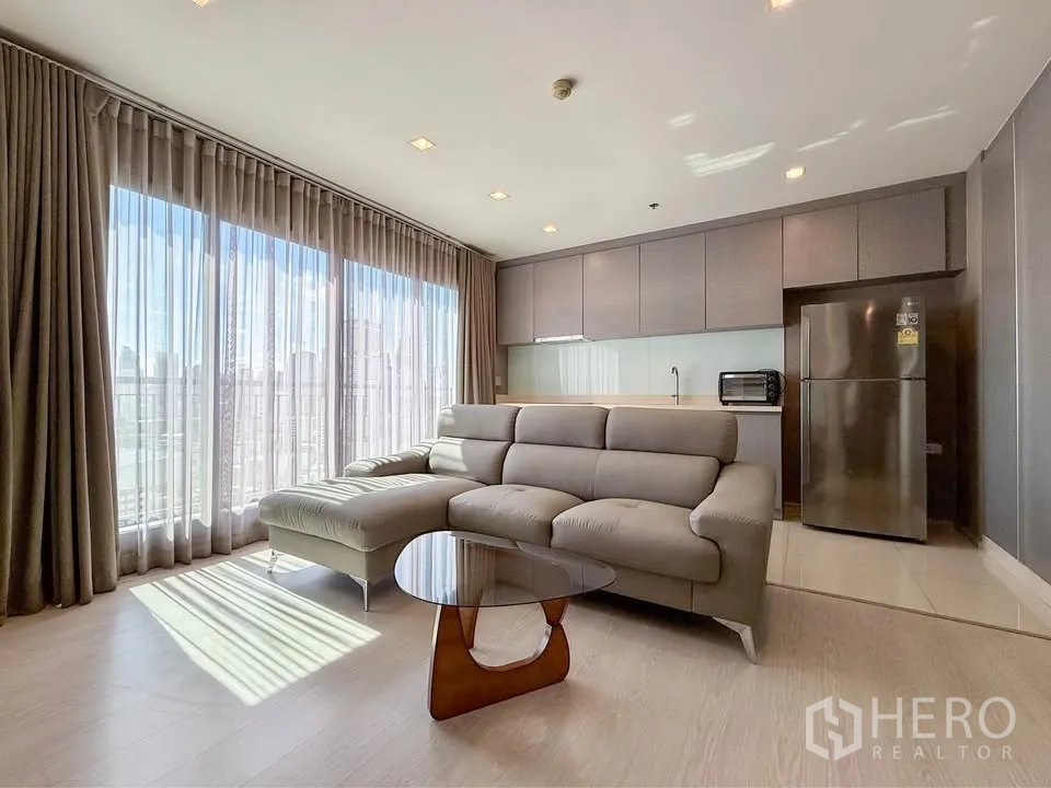 Condominium for rent in Khlong Toei, Bangkok - Sunlit living area featuring sectional sofa, coffee table and grey kitchen.