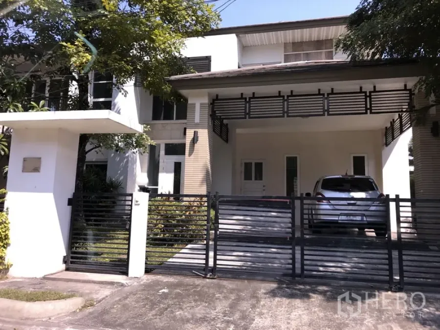 บ้าน ขายในSaphan Sung, Bangkok - บ้านเดี่ยวสองชั้นย่านสะพานสูง กรุงเทพฯ มีกำแพงรั้ว ประตูเลื่อน โรงรถมีหลังคาจอดได้ 2 คัน และระเบียงชั้นบนใต้ร่มไม้