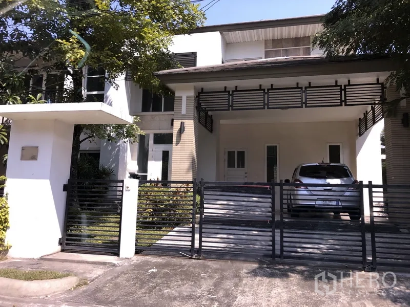 บ้าน ขายในSaphan Sung, Bangkok - บ้านเดี่ยวสองชั้นย่านสะพานสูง กรุงเทพฯ มีกำแพงรั้ว ประตูเลื่อน โรงรถมีหลังคาจอดได้ 2 คัน และระเบียงชั้นบนใต้ร่มไม้