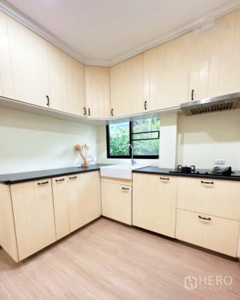 บ้าน ขายในLam Luk Ka, Pathum Thani - ครัวรูปตัว U ตู้ลายไม้สีอ่อน ท็อปสีดำ เตาแก๊ส และหน้าต่างระบายอากาศ