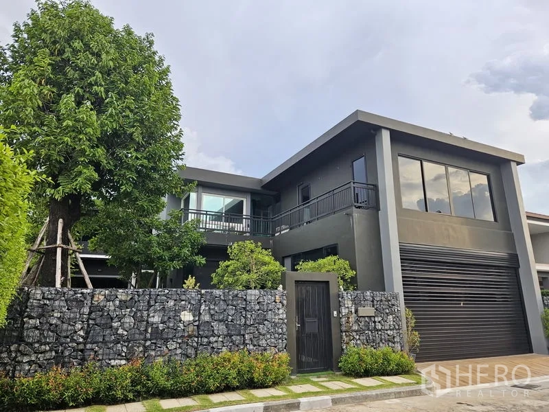 Detached House for sale in Thawi Watthana, Bangkok - Modern two-storey detached house with dark facade, large windows and a stone boundary wall in Thawi Watthana.