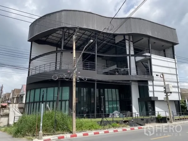 展厅 出租在Lat Phrao, Bangkok - 曼谷拉抛四层展示厅建筑，弧形金属屋顶与整面玻璃立面，位于街角。