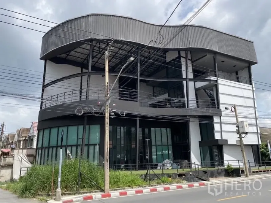 展厅 出租在Lat Phrao, Bangkok - 曼谷拉抛四层展示厅建筑，弧形金属屋顶与整面玻璃立面，位于街角。