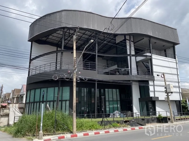 展厅 出租在Lat Phrao, Bangkok - 曼谷拉抛四层展示厅建筑，弧形金属屋顶与整面玻璃立面，位于街角。