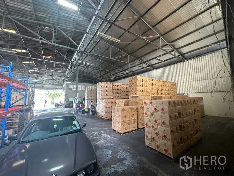 Warehouse for rent in Suan Luang, Bangkok - Wide storage hall with stacked cartons and indoor vehicle parking.