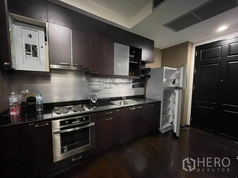 Condominium for rent or sale in Watthana, Bangkok - Fitted kitchen with dark cabinets, electric cooktop, oven, double sink and fridge.