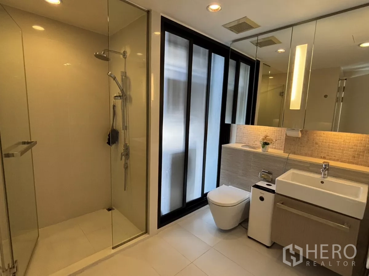 Condominium for sale in Watthana, Bangkok - Contemporary bathroom with glass-enclosed shower, vanity, and backlit mirror.