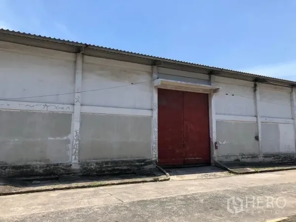 คลังสินค้า ให้เช่าในLat Krabang, Bangkok - ด้านหน้าโกดังพร้อมประตูโหลดสีแดงขนาดใหญ่ ทางลาดคอนกรีตและหลังคาลอนเหล็ก