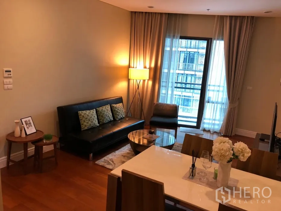 公寓 出租或出售在Khlong Toei, Bangkok - 客厅配落地窗帘与阳台玻璃门，沙发旁设餐桌，灯光温暖。