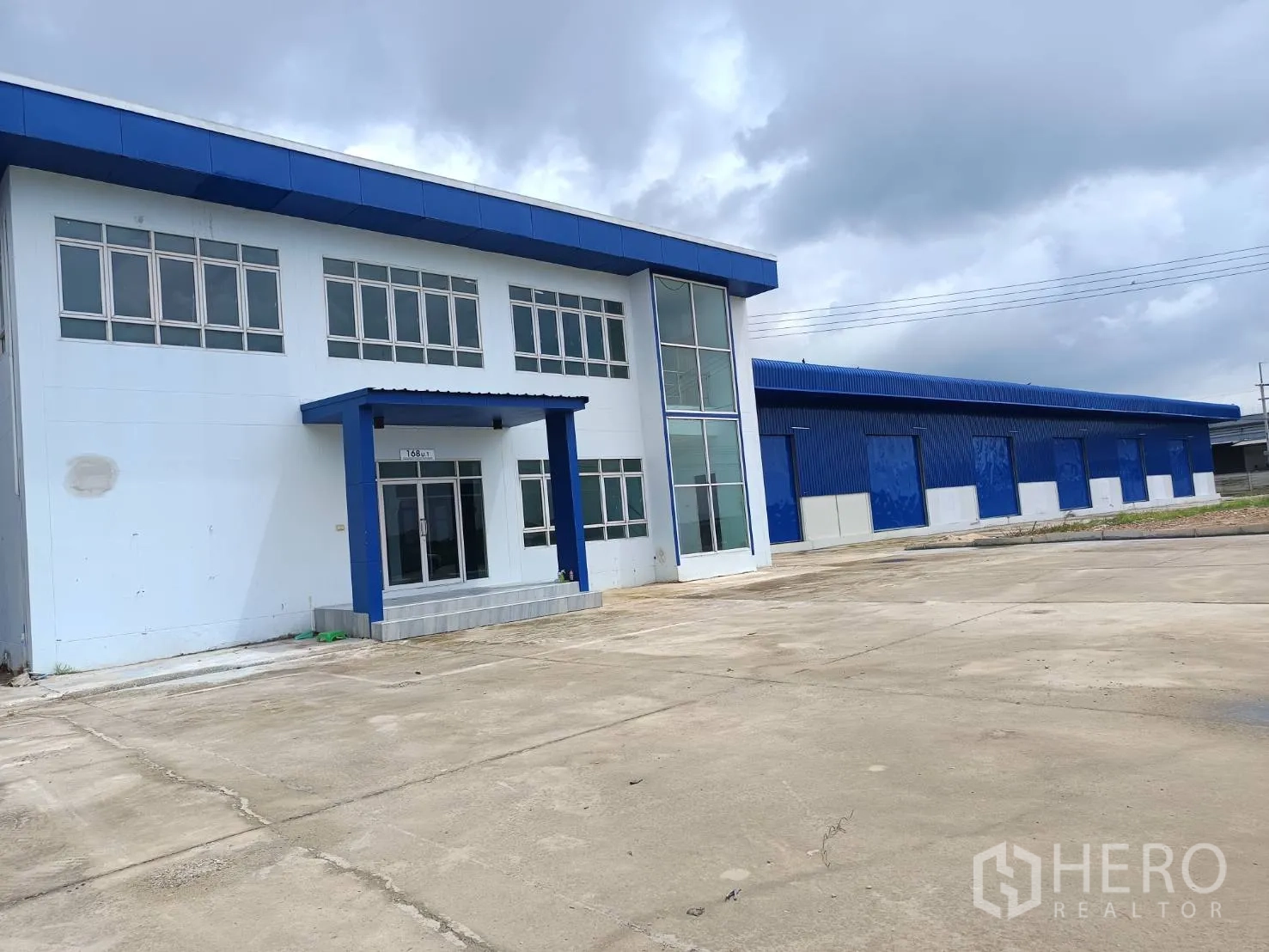 Warehouse for rent in Bang Len, Nakhon Pathom - Office building entrance beside long warehouse block on expansive paved yard.