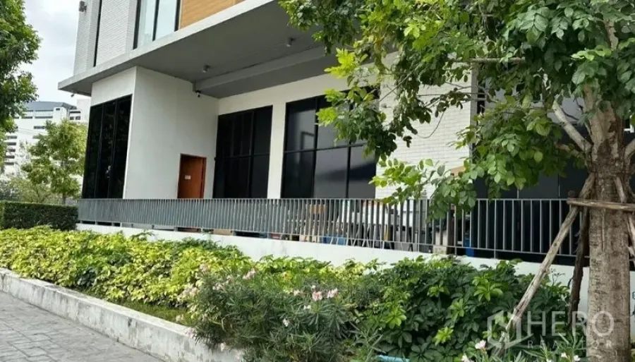 零售空间 出租 - 商铺侧立面，栏杆与大树掩映，宽大玻璃与灌木景观