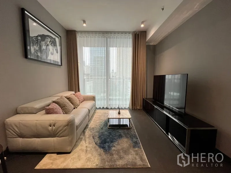 Condominium for rent in Bang Rak, Bangkok - Cozy living area with sofa, rug, TV unit and balcony-style window.