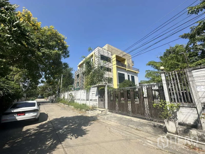 Home Office for sale in Lam Luk Ka, Pathum Thani - Gated property on a quiet, tree-lined residential street with perimeter wall and driveway