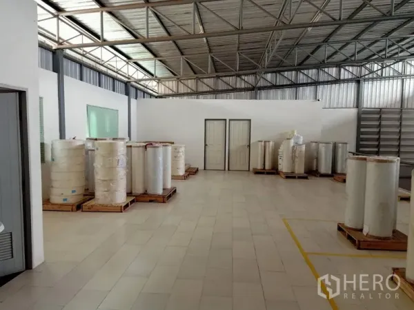 คลังสินค้า ให้เช่าในBang Kapi, Bangkok - พื้นที่ภายในโกดัง เพดานโครงเหล็ก พื้นกระเบื้อง ผนังกั้นสีขาว และม้วนวัสดุวางบนพาเลท