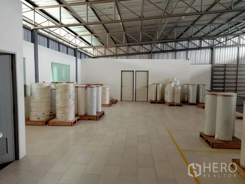 คลังสินค้า ให้เช่าในBang Kapi, Bangkok - พื้นที่ภายในโกดัง เพดานโครงเหล็ก พื้นกระเบื้อง ผนังกั้นสีขาว และม้วนวัสดุวางบนพาเลท