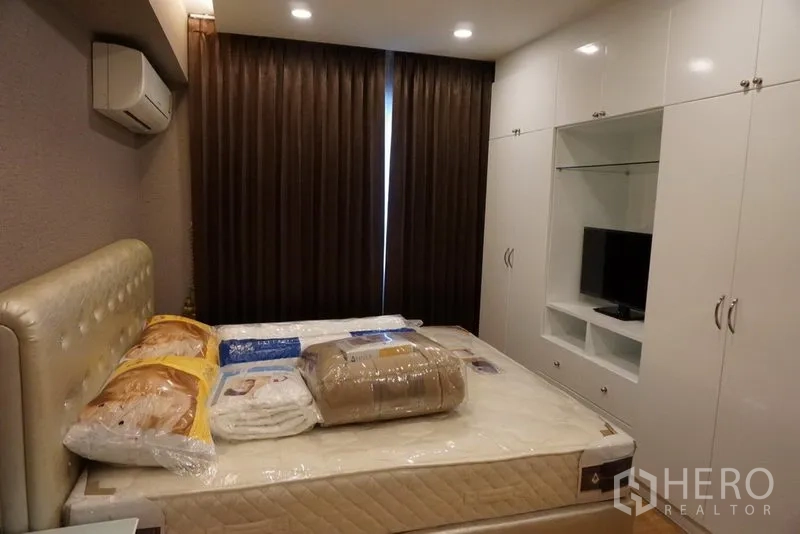 Condominium for rent in Watthana, Bangkok - Cozy bedroom with padded headboard, blackout curtains and glossy white built‑in wardrobes.