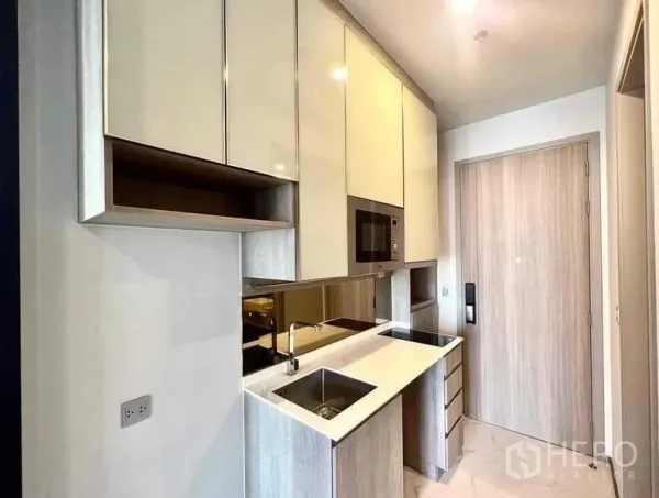 Condominium for sale - Compact modern kitchenette with glossy cabinets, built-in microwave, sink and cooktop by the entry.