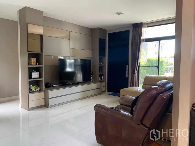 Detached House for rent or sale in Bang Phli, Samut Prakan - Living room with built-in media wall, large TV, leather recliner and floor-to-ceiling window.