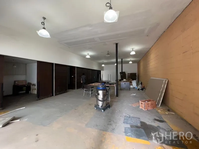 Warehouse for rent in Suan Luang, Bangkok - Long warehouse bay with multiple pendant fixtures, partitioned rooms along one side, and a clear loading aisle.