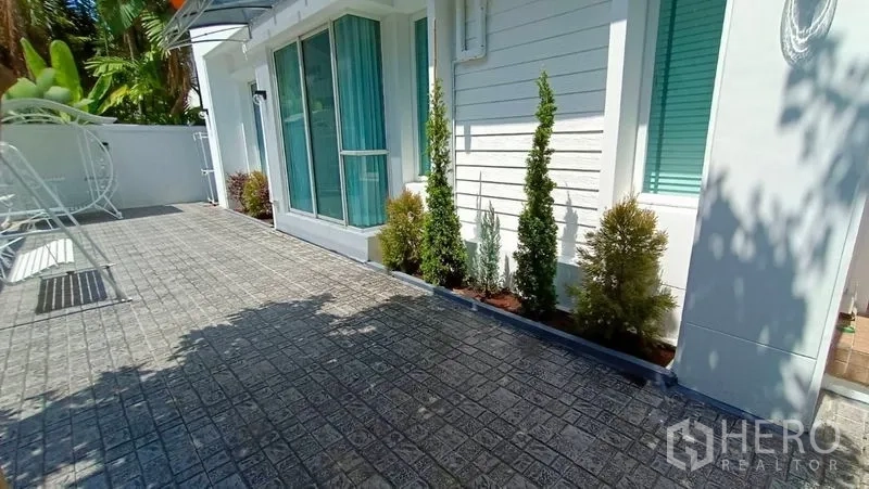 独立式住宅 出租在Prawet, Bangkok - 侧院铺砖露台，落地推拉窗与蓝色窗帘，小灌木