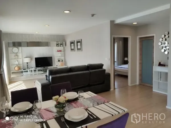 Condominium for rent or sale in Pathum Wan, Bangkok - Spacious open-plan living–dining area with TV feature wall and doorway to bedroom, filled with natural light.
