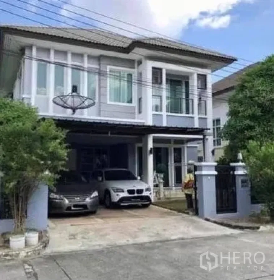 Detached House for sale in Khan Na Yao, Bangkok - Two-storey detached house exterior with gated driveway, covered carport for two cars, and balcony.