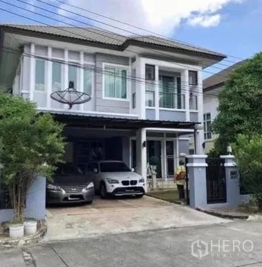 Detached House for sale in Khan Na Yao, Bangkok - Two-storey detached house exterior with gated driveway, covered carport for two cars, and balcony.