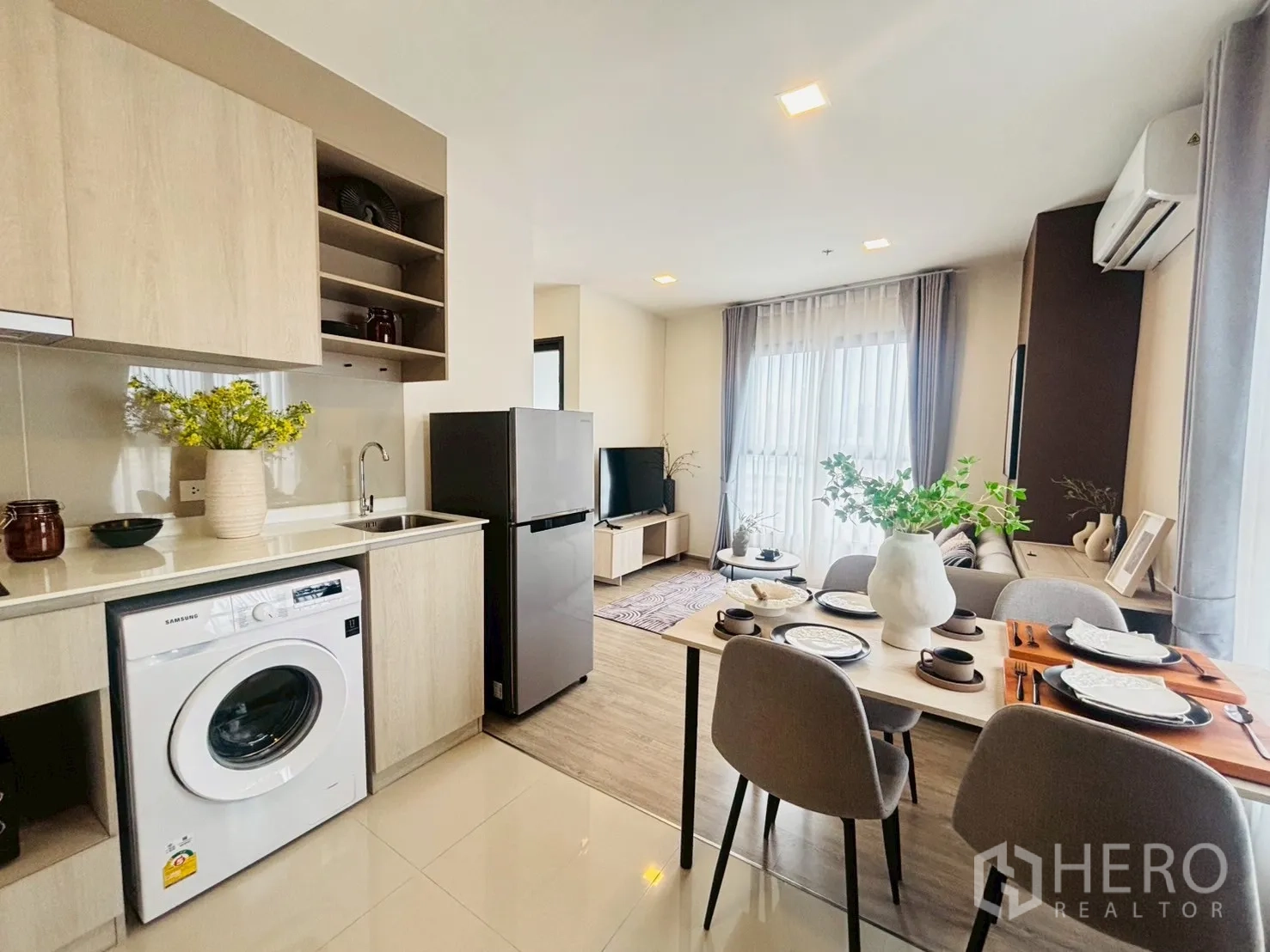 Condominium for rent in Watthana, Bangkok - Compact modern kitchenette with light wood cabinets, sink, and a set dining table in a bright living space.