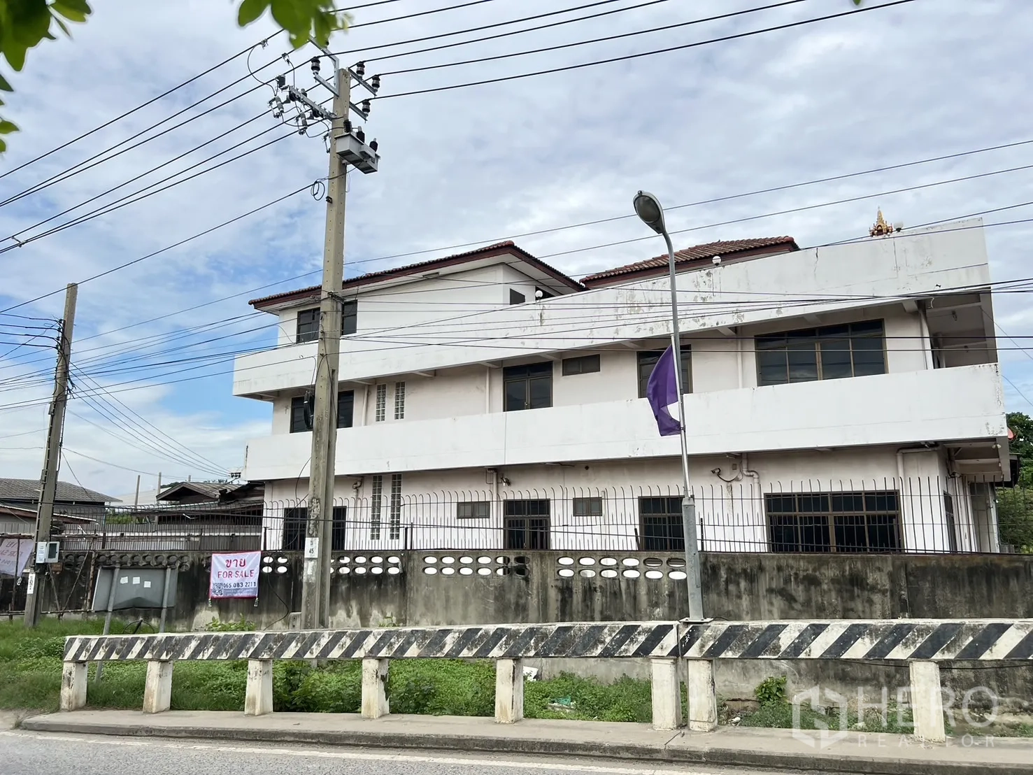 Home Office for sale in Phra Pradaeng, Samut Prakan - Streetside perspective of the building with road barrier and greenery.