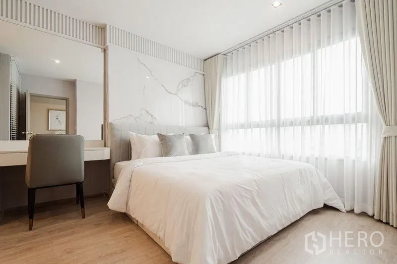 Condominium for rent - Sunlit bedroom with large bed, marble accent wall and full-height curtains.