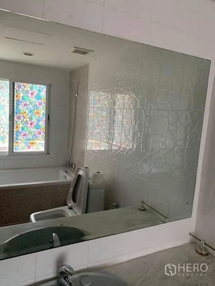联排别墅 for rent in Watthana, Bangkok - 浴室配浴缸、坐便器、大镜子和带彩色贴膜的窗户。