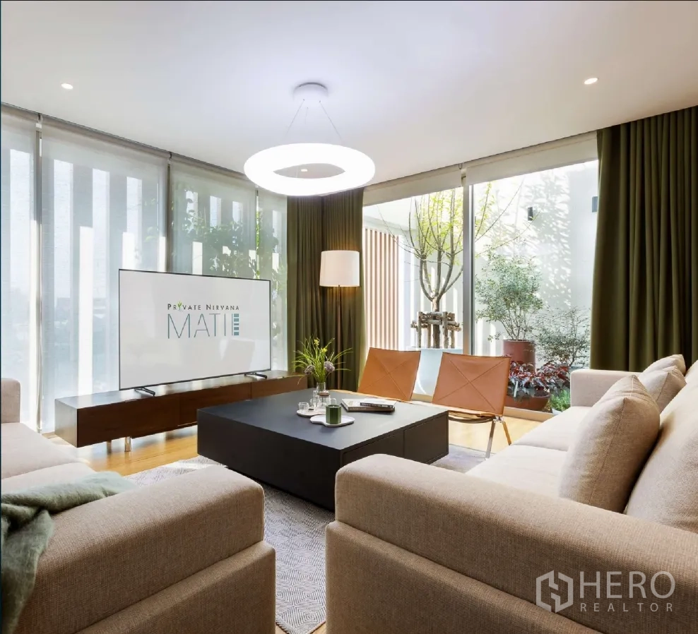 家庭办公室 for rent or sale in Bang Khen, Bangkok - 明亮客厅配大沙发、茶几与落地玻璃，可眺望室外绿植。