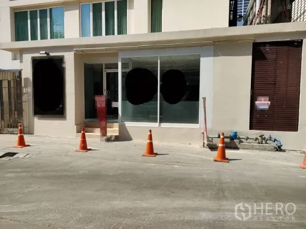 零售空间 出租在Khlong Toei, Bangkok - 临街一层商铺外立面，大片玻璃橱窗、台阶入口与路边交通锥，位于曼谷空堤区