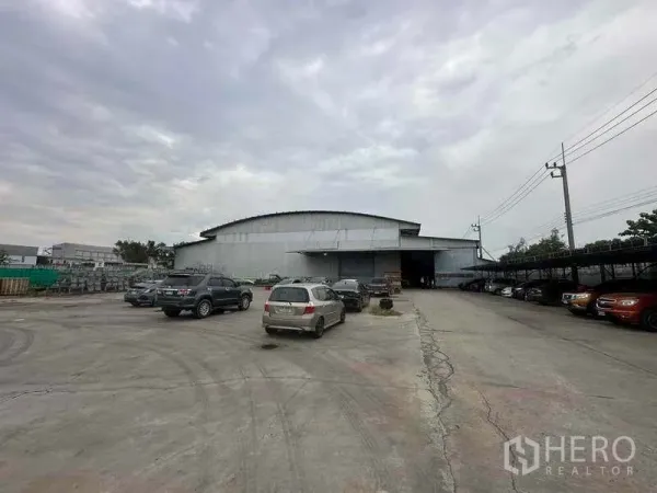 Factory for rent in Pathum Thani - Front approach to the warehouse showing loading bays, parked cars and roadside power lines.