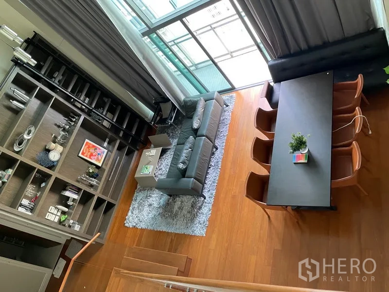 คอนโด ให้เช่าในKhlong Toei, Bangkok - มุมสูงของพื้นที่นั่งเล่น–รับประทานอาหารเพดานสูง ผนังกระจกเต็มบาน โซฟาสีเทาและโต๊ะยาว พื้นไม้