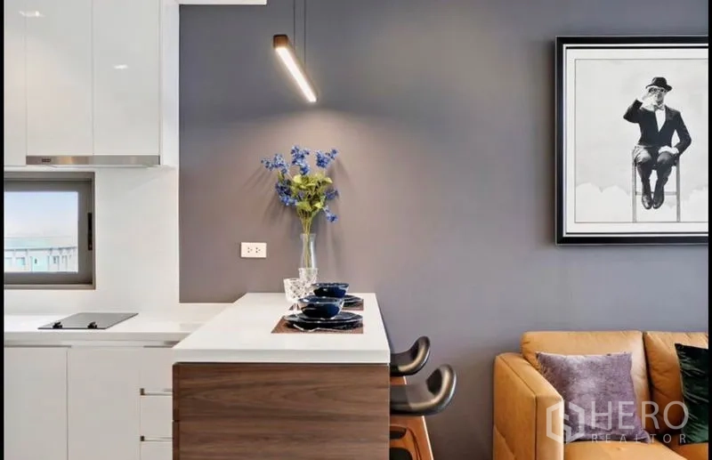 Condominium for rent in Bang Rak, Bangkok - Compact kitchen with breakfast bar, pendant light and sleek cabinetry beside a sofa.