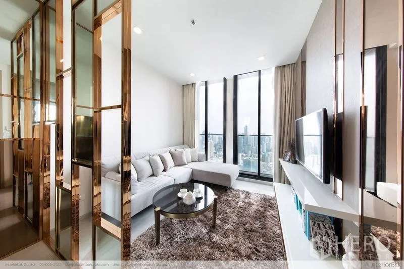 Condominium for rent in Pathum Wan, Bangkok - Bright living room with L-shaped sofa, shag rug, TV wall and floor-to-ceiling windows overlooking the Bangkok skyline.